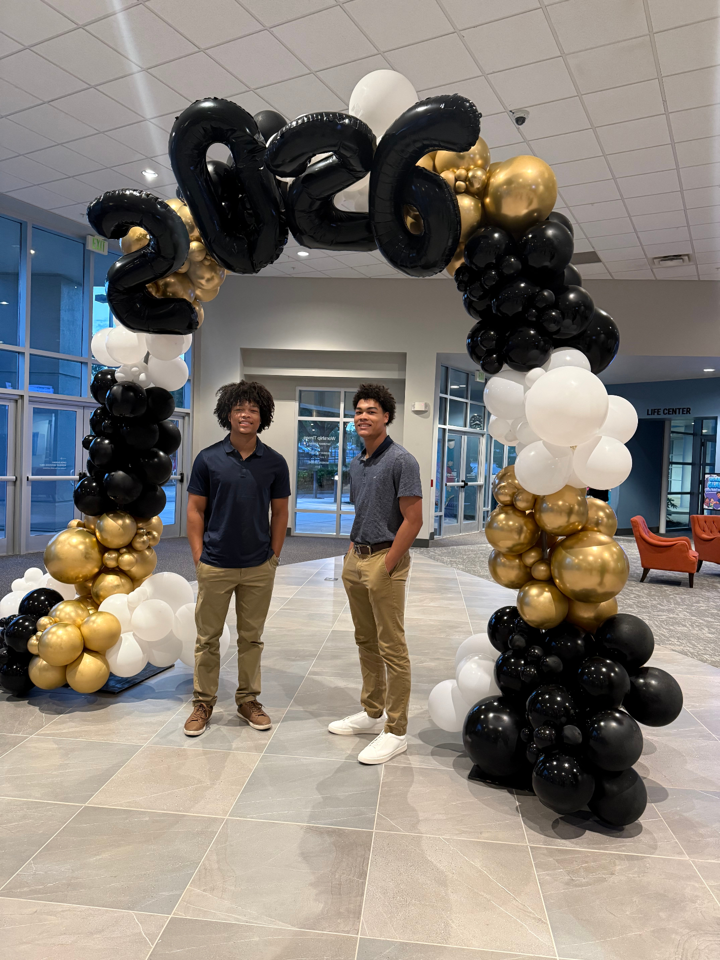 The twin brothers and founders of Lendova standing beneath a black and gold 2026 balloon arch